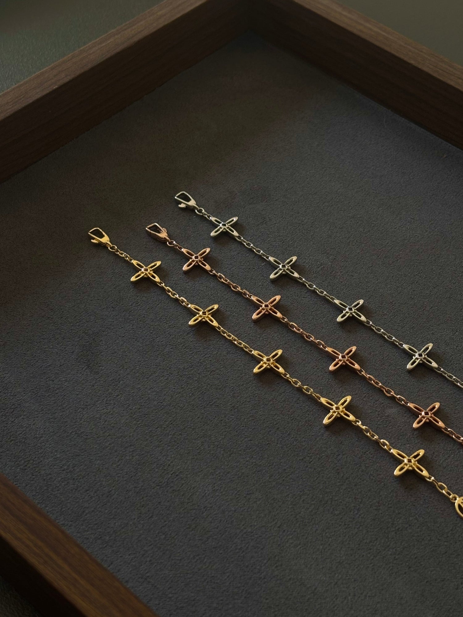 Drei Celestial Armbänder in Gold, Roségold und Silber von Ovis & Co auf dunklem Untergrund, filigranes Design mit Kreuzanhängern.