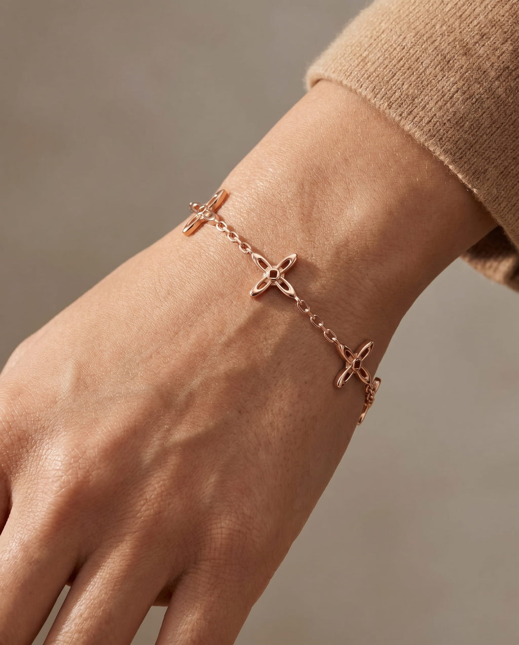 Ovis & Co. Celestial Armband Roségold – Edelstahlarmband mit 5 filigranen Kreuz-Anhängern in warmem Roségold, getragen zu beigem Strickpullover, designed in Frankfurt
