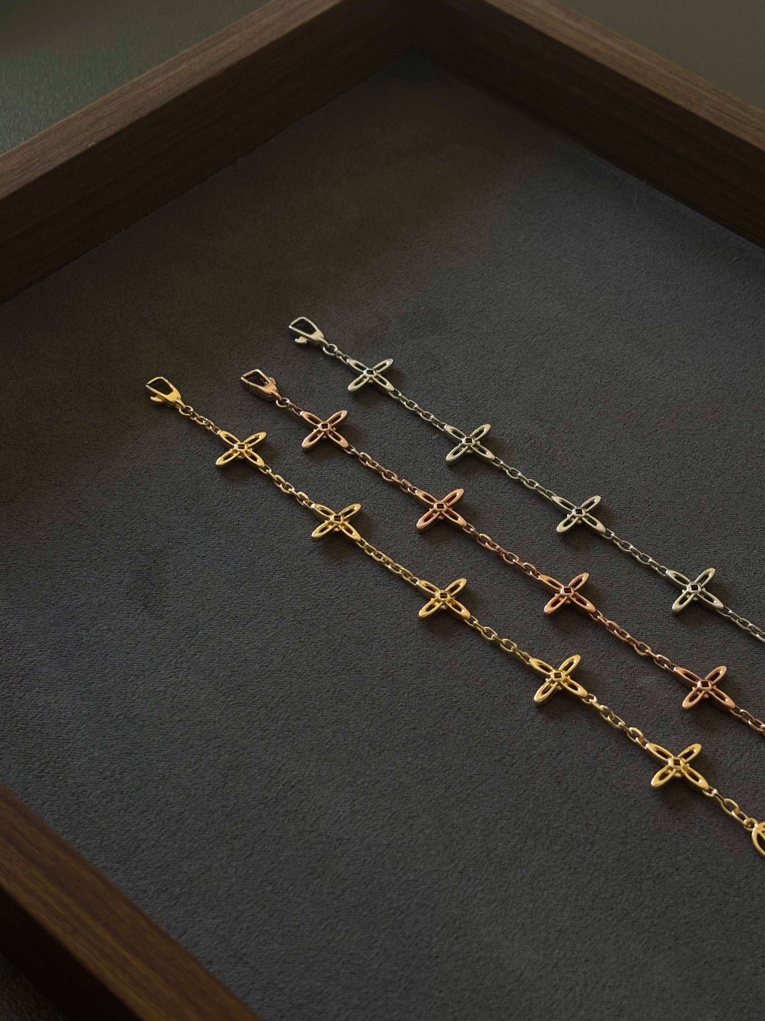 Drei Celestial Armbänder in Gold, Roségold und Silber von Ovis & Co auf dunklem Untergrund, filigranes Design mit Kreuzanhängern.