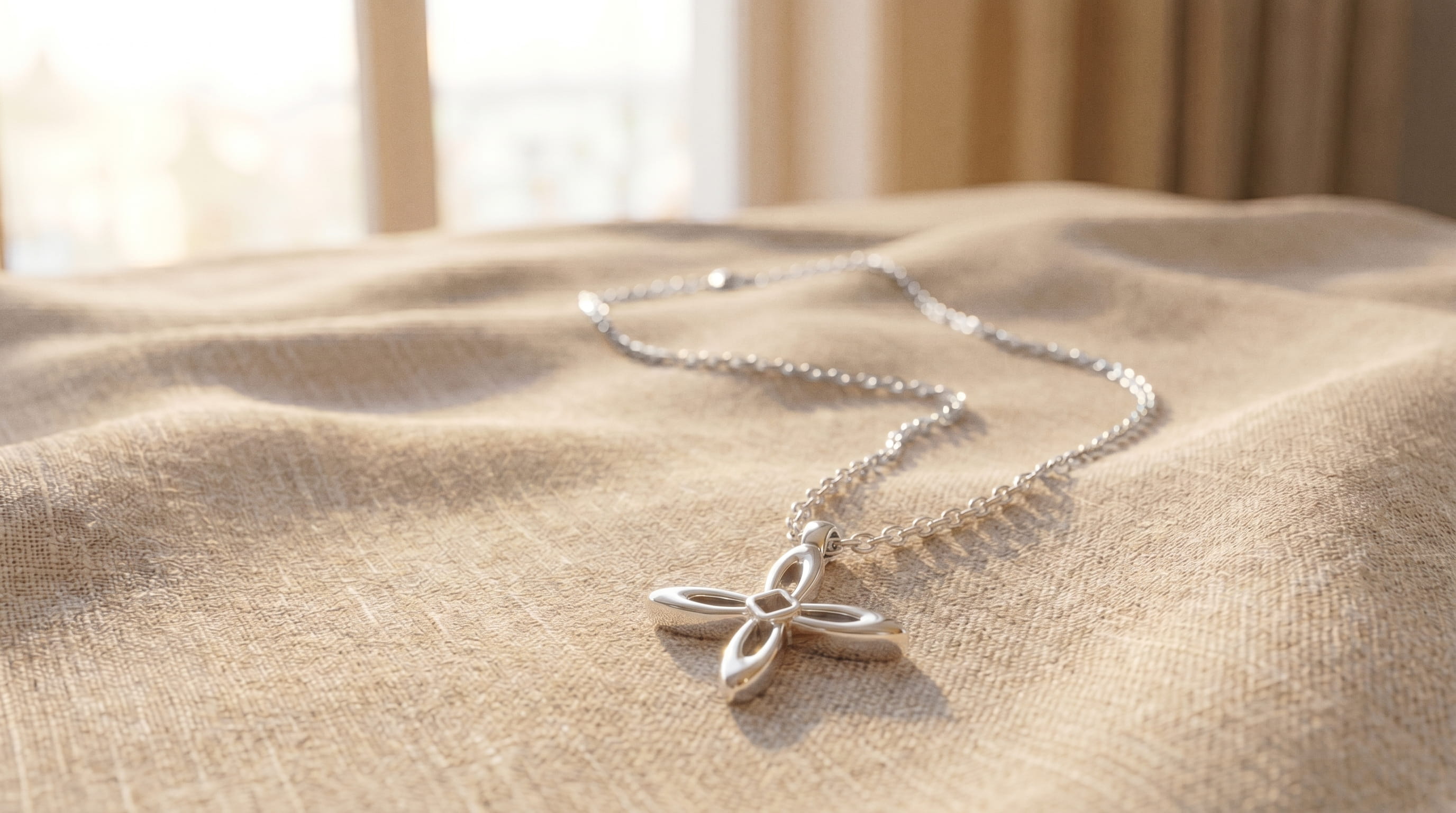 Ovis & Co. Celestial Kette Silber – minimalistische Edelstahlkette mit filigranem Kreuz-Anhänger auf natürlichem Leinenstoff im Sonnenlicht, designed in Frankfurt