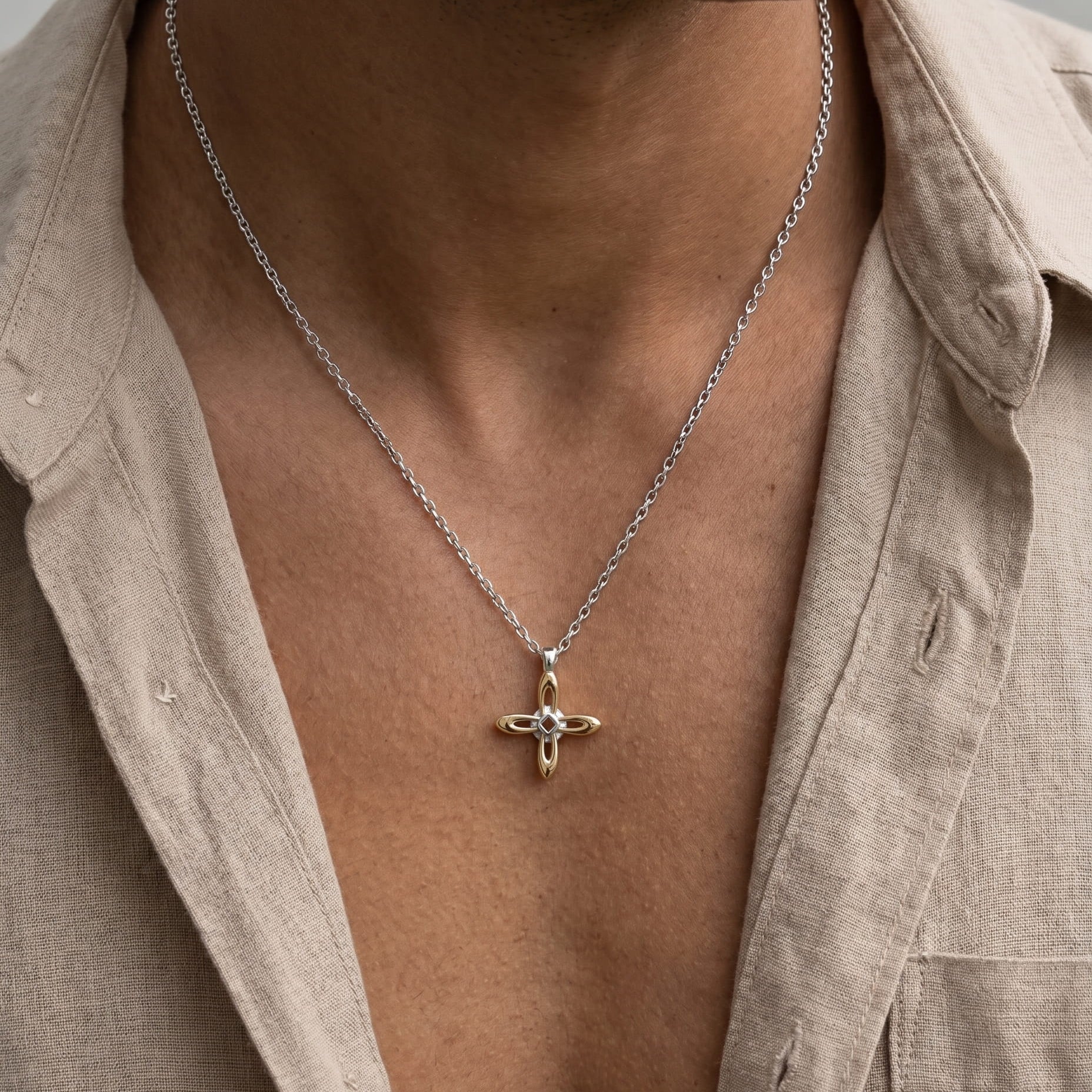 Ovis & Co. Celestial Kette Two-Tone – Edelstahlkette mit filigranem Kreuz-Anhänger in Silber und Gold, getragen von Mann mit offenem beigen Leinenhemd, designed in Frankfurt