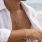 Ovis & Co. Celestial Set Two-Tone – Edelstahlkette mit goldenem Anhänger und Armband mit 5 filigranen Anhängern in Silber und Gold, getragen von Mann am Strand zu weißem Leinenhemd, designed in Frankfurt
